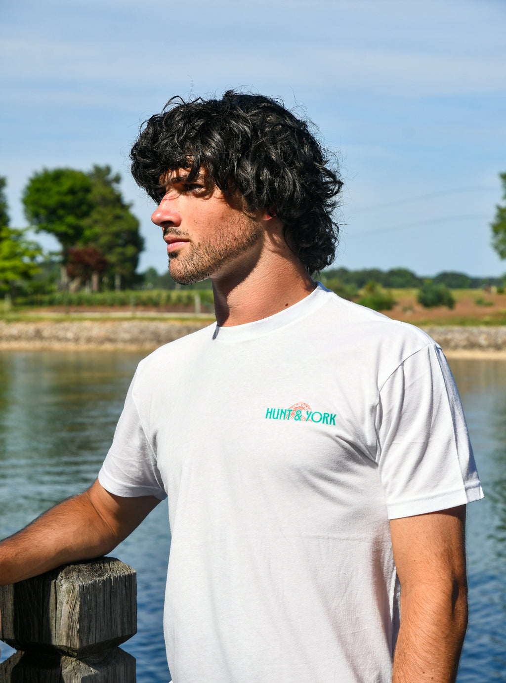 Man wearing a white t-shirt with a logo by a body of water